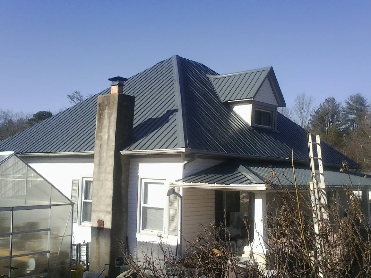 Dark blue standing seam metal roof on a white farmhouse with dormer — Slate & Tile Roof Repair by Roofing Brothers in Seneca Falls