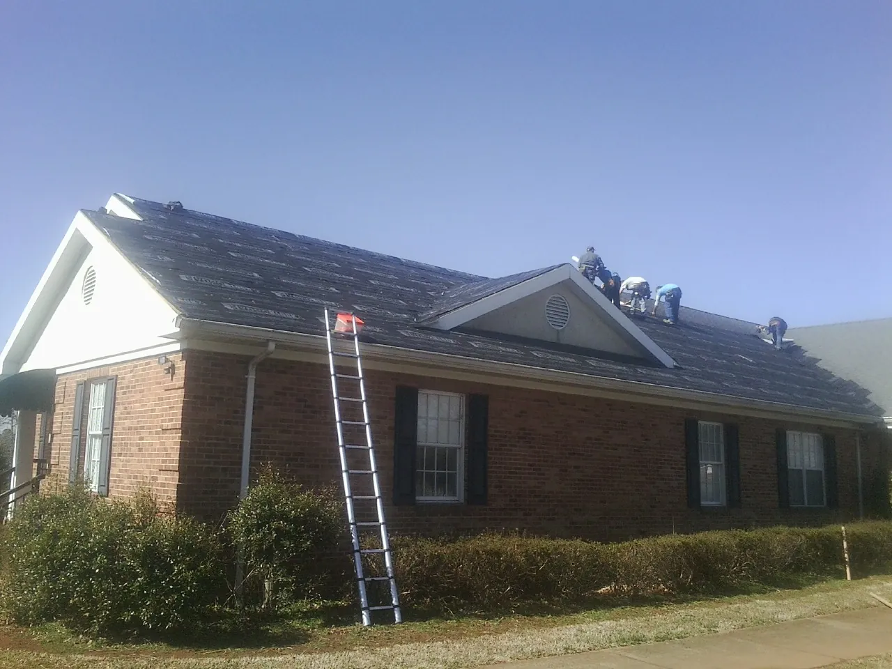 Crew tearing shingles off a brick ranch roof with a ladder set — Emergency Roof Repair work by our crew in Seneca Falls