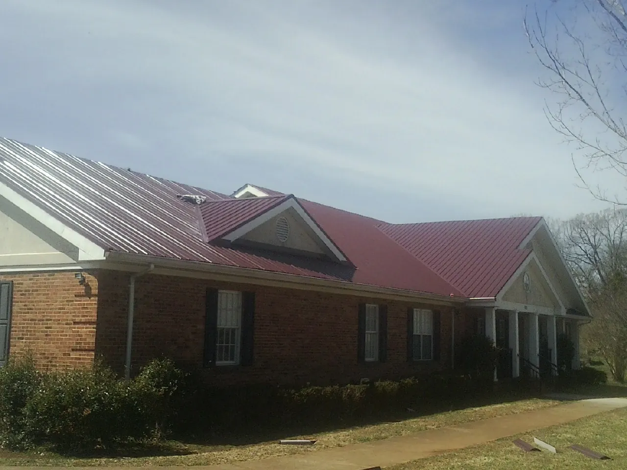 Red metal roof with gabled entries on a long brick building, from a Hail Damage Roof Repair job in Seneca Falls