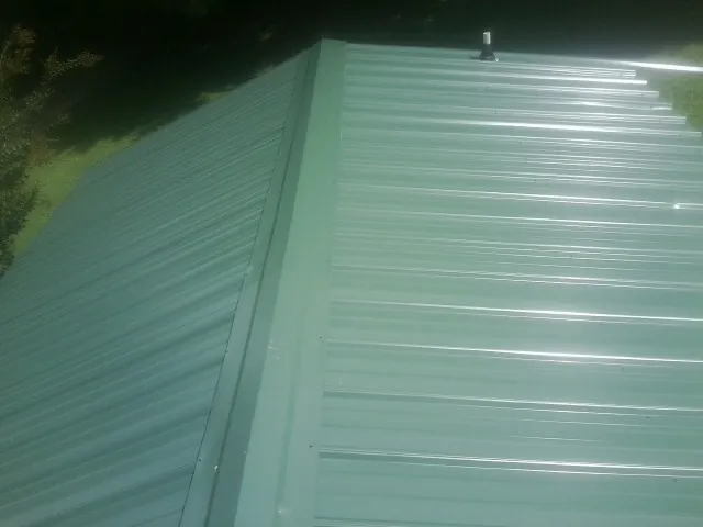 New green metal panels meeting at the ridge of a roof — Flat Roof Repair work by our crew in Seneca Falls