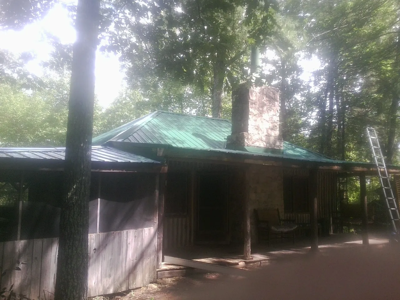 Green metal roof and stone chimney above a log cabin porch in Seneca Falls