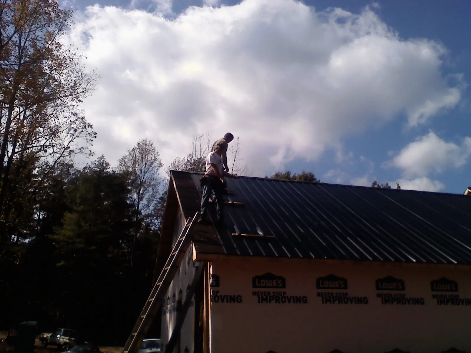 Roofer fastening dark metal panels high against a cloudy sky, from a Roof Inspection job in Seneca Falls