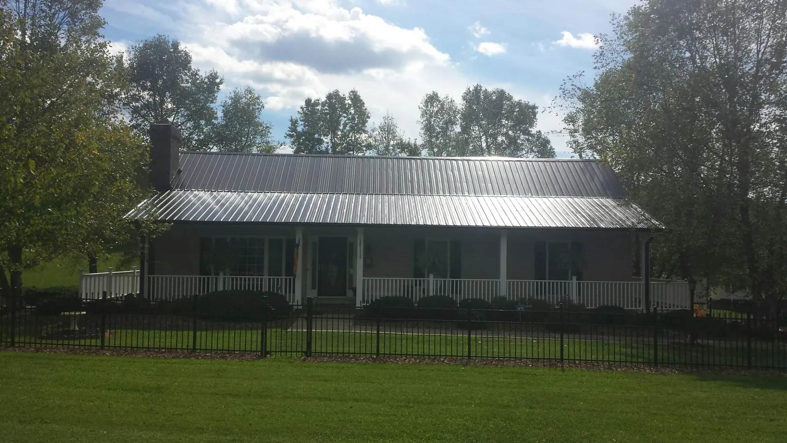 Gray metal roof on a brick ranch with a full width front porch — Gutter Guard Installation work by our crew in Seneca Falls