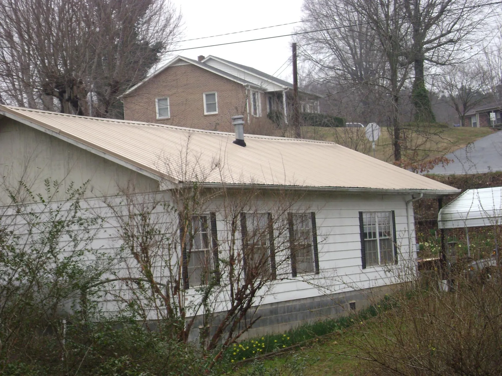 Tan metal roof on a white sided house set into a hillside — Commercial Roofing by Roofing Brothers in Seneca Falls