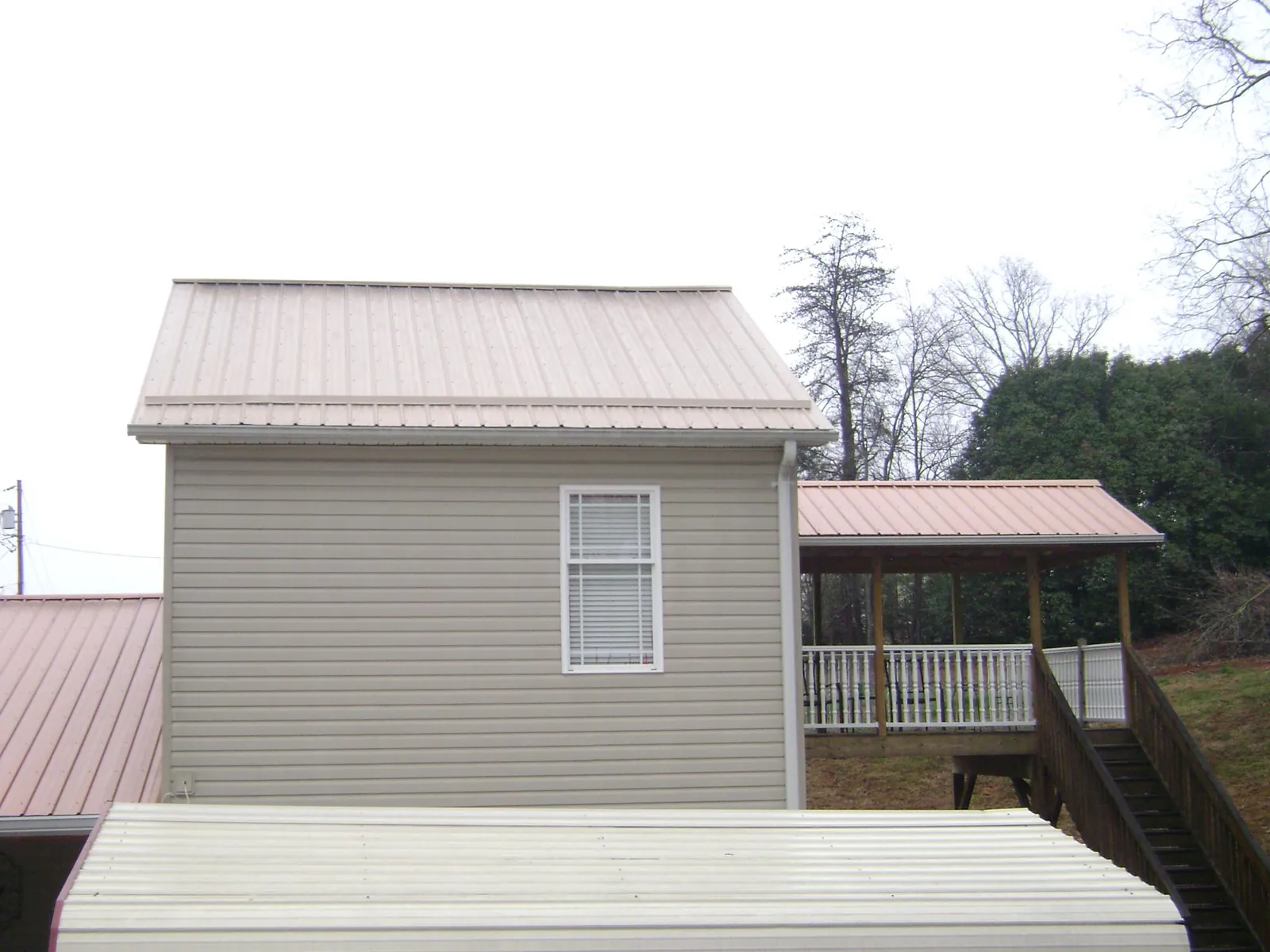 Tan metal roofs on a two story addition and attached porch, from a Roof Replacement job in Seneca Falls