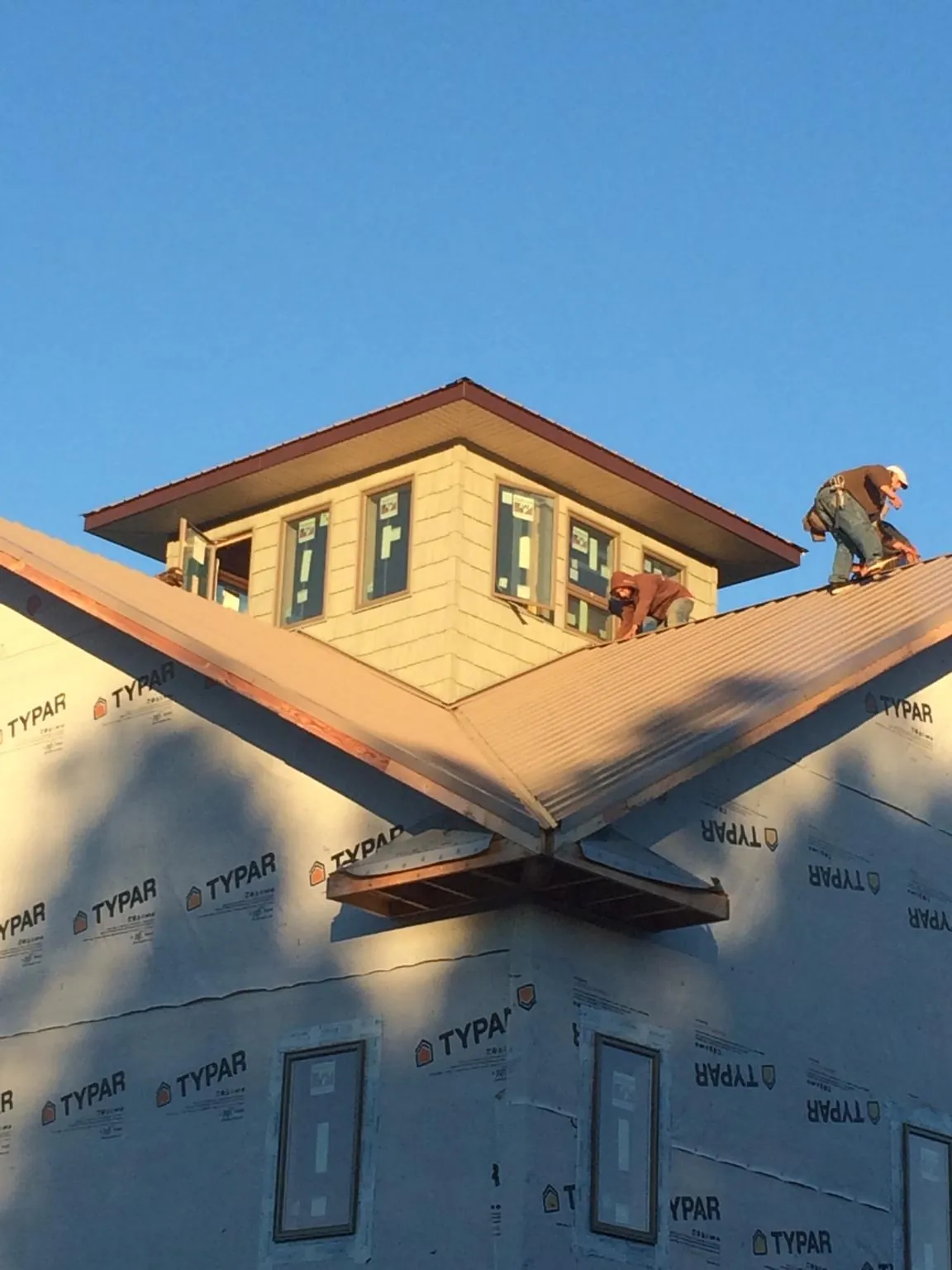 Roofers working around a rooftop cupola on a new metal roof at sunset — Roof Waterproofing in Seneca Falls by Roofing Brothers